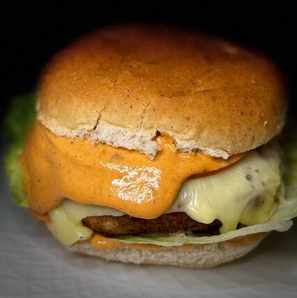 Air-fried Karahi Paneer Burger with melted cheese and creamy chipotle sauce on a whole wheat bun.