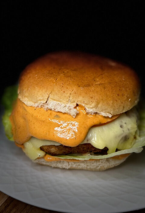Air-fried Karahi Paneer Burger with melted cheese and creamy chipotle sauce on a whole wheat bun.
