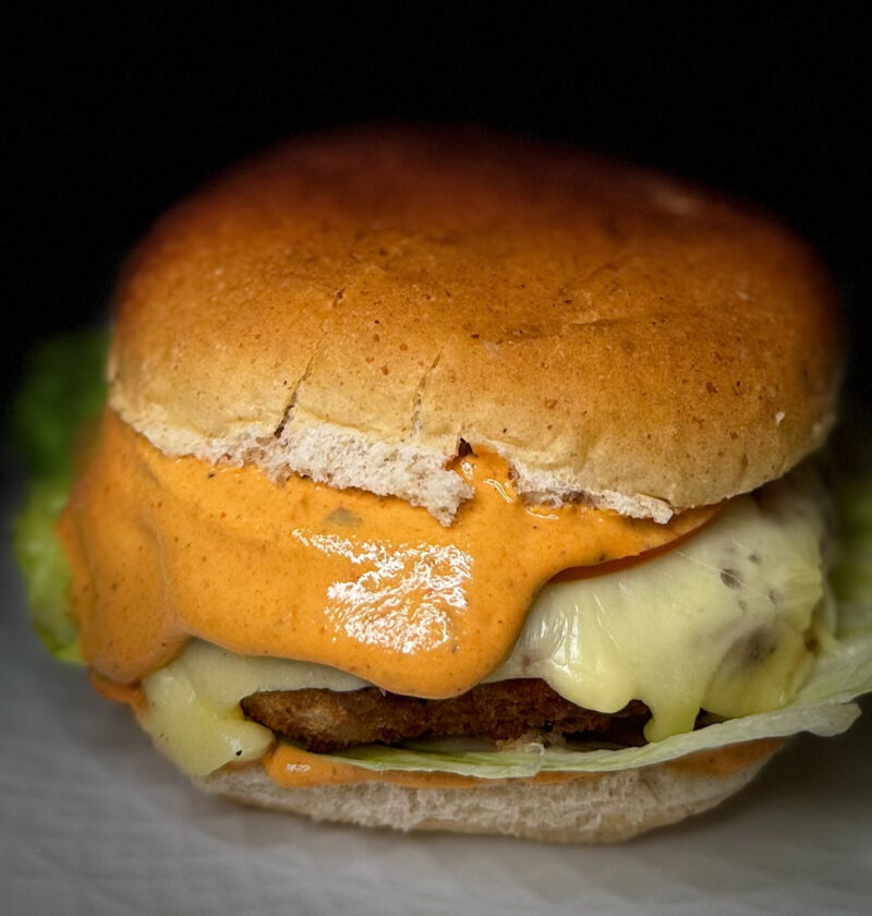 Air-fried Karahi Paneer Burger with melted cheese and creamy chipotle sauce on a whole wheat bun.
