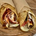 Paneer shawarma wraps loaded with charred paneer, spiced pickled onions, and creamy garlic sauce on a wooden board.
