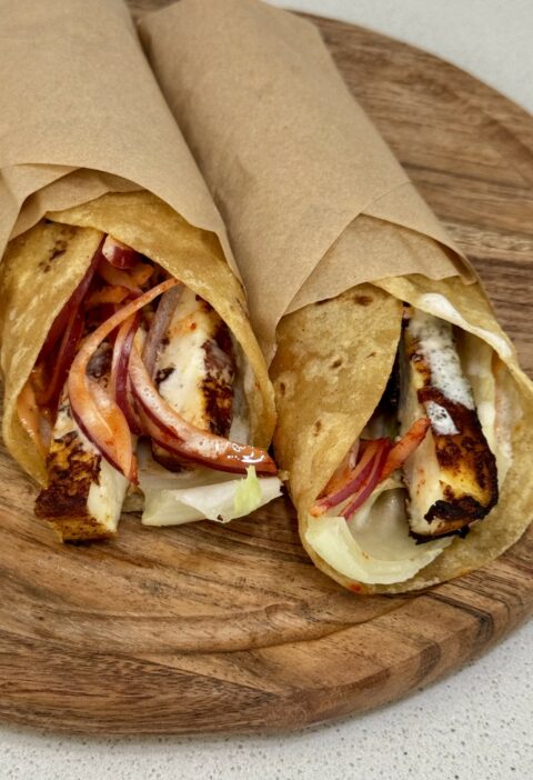 Paneer shawarma wraps loaded with charred paneer, spiced pickled onions, and creamy garlic sauce on a wooden board.