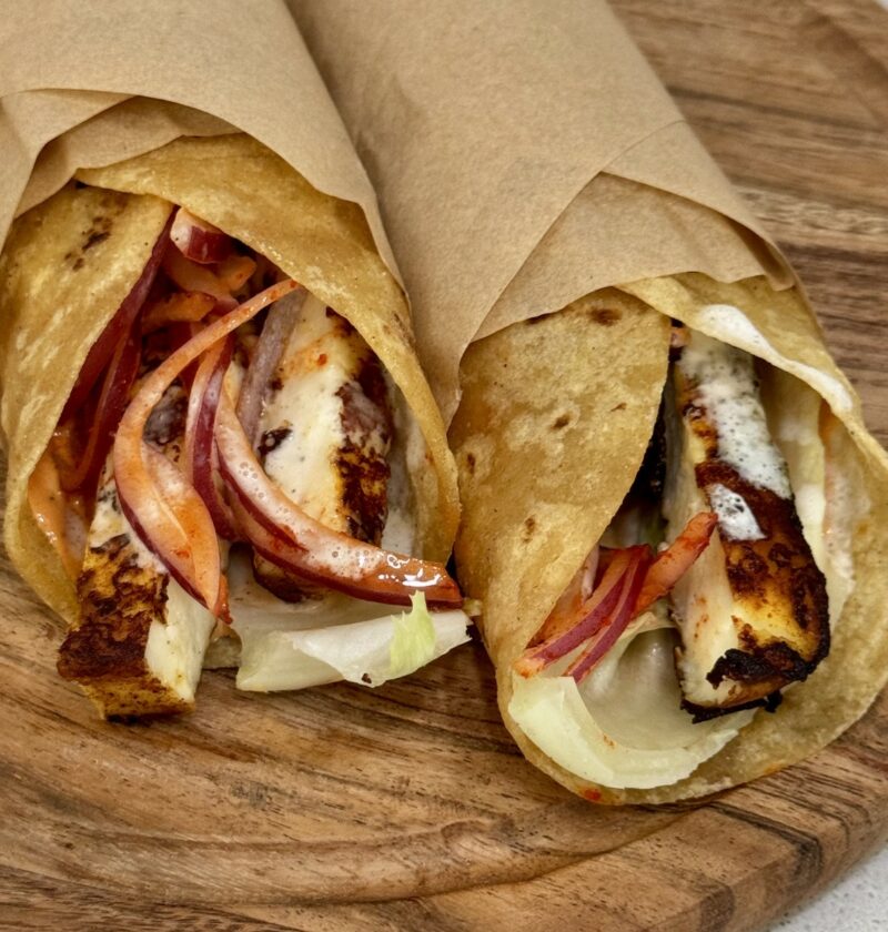 Paneer shawarma wraps loaded with charred paneer, spiced pickled onions, and creamy garlic sauce on a wooden board.
