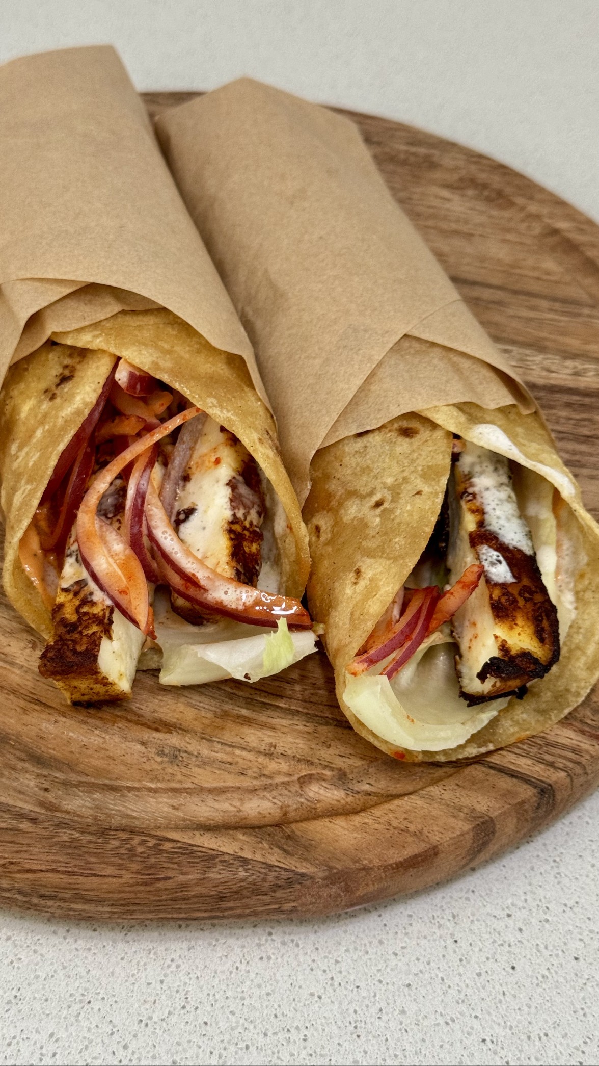 Paneer shawarma wraps loaded with charred paneer, spiced pickled onions, and creamy garlic sauce on a wooden board.