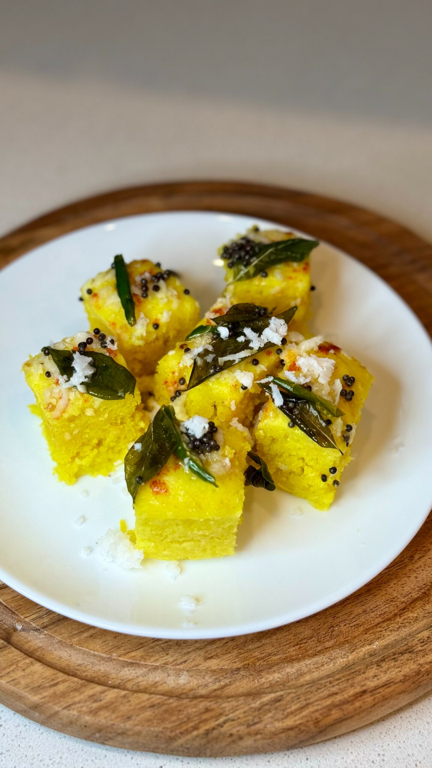 Soft, spongy yellow moong dal dhokla squares garnished with mustard seeds, fresh curry leaves, and grated coconut