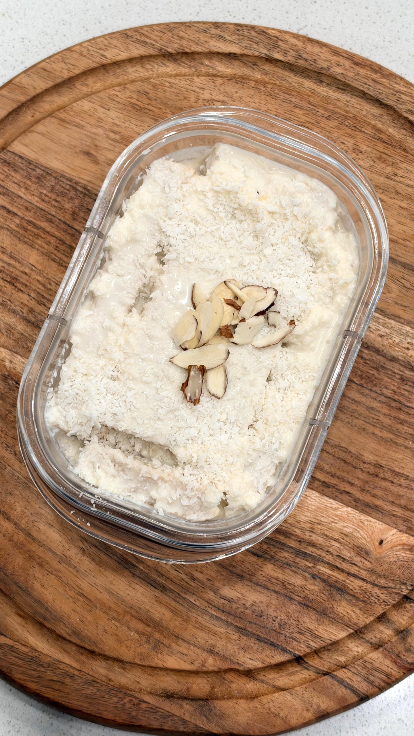 High-protein coconut bread pudding topped with chopped almonds in a glass container